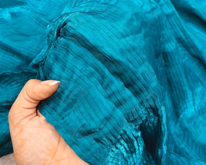 Close-up of blue fabric with a hand holding it, on a light background