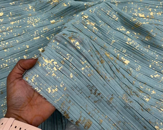 Close-up of pleated fabric with gold accents held by a hand wearing a pink watch.