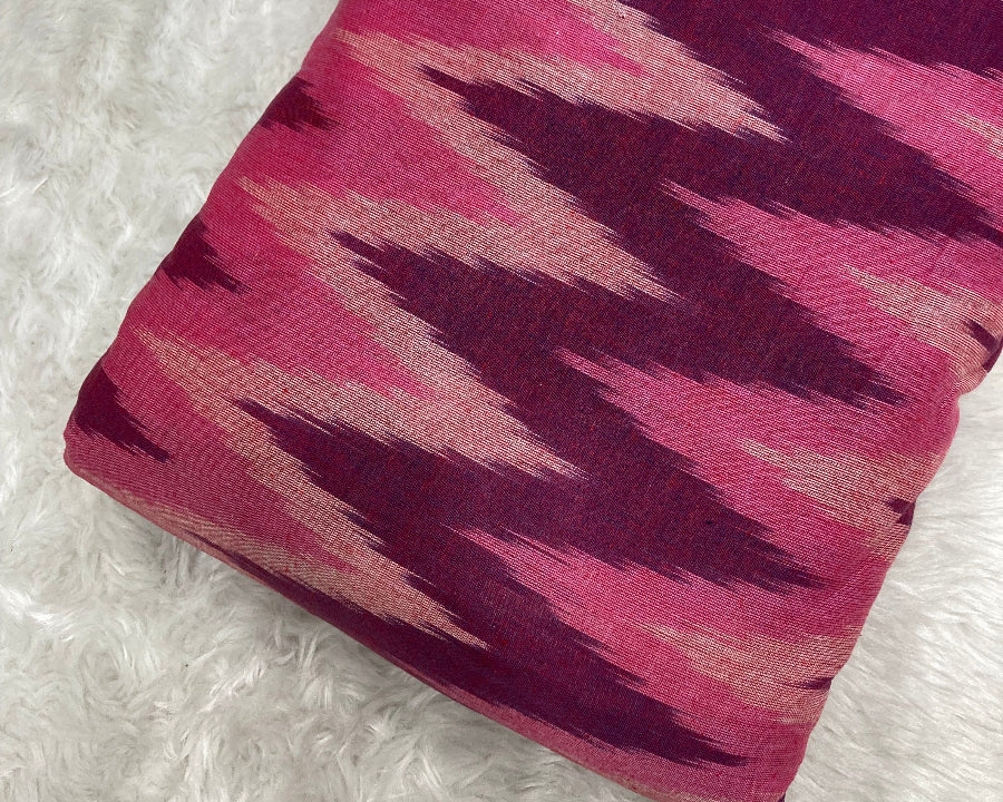 Roll of fabric with pink and purple ikat pattern on a white textured background