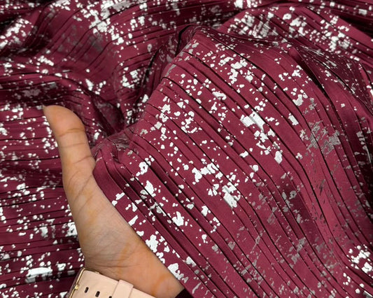 Close-up of maroon fabric with silver glitter, held by a hand wearing a beige bracelet.